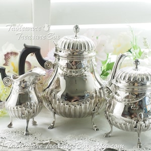May include: A silver tea set comprising a teapot, creamer and sugar bowl. The set features a traditional design with intricate detailing and three legs on each piece.