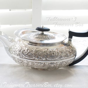 May include: A silver teapot with an ornate floral design and a black wooden handle. The teapot has a round body and a lid with a black knob. The text "Tableware Treasure Box" is visible in the image.