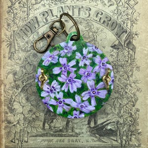 Porte-clés presse-fleurs unique en son genre, peint à la main, avec phlox rampant. Il tient dans votre poche ou se fixe à votre sac ou à votre porte-clés.