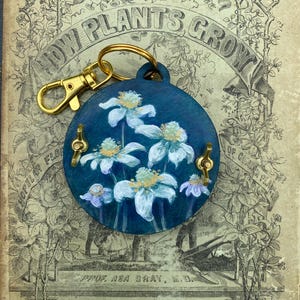 Le porte-clés presse-fleurs peint à la main en fait partie. Il tient dans votre poche ou se fixe à votre sac ou à votre porte-clés.