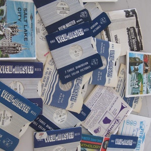 Könnte beinhalten: Eine Sammlung von Vintage View-Master-Rollen mit bunten Etiketten und Bildern. Die Rollen zeigen verschiedene Themen, darunter "Salt Lake City", "Mount Rushmore", "Vereinte Nationen" und "Wunder der Welt".