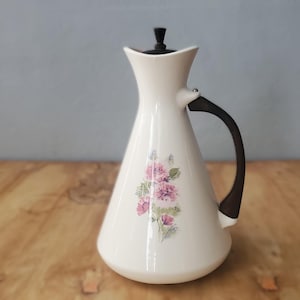 May include: White ceramic pitcher with a floral design featuring pink and purple flowers. The pitcher has a black handle and a black lid.