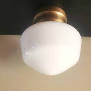 May include: A flush mount ceiling light fixture featuring a spherical white glass globe shade attached to a circular brass-toned metal base. The fixture is mounted against a flat black surface, providing a clean and simple lighting design.