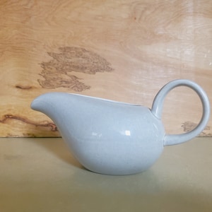 May include: A light gray ceramic gravy boat with a rounded body and a curved handle.