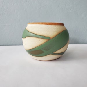 May include: A small, round ceramic planter with a white base and green and brown abstract designs.