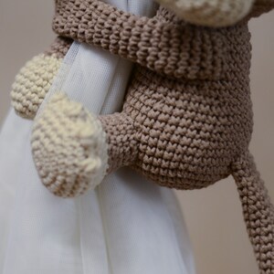 May include: A brown crocheted monkey toy with a cream-colored face and hands, holding onto a white curtain.