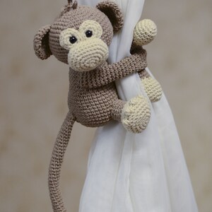 Adorable stuffed monkey curtain holder for nursery windows. Soft knitted animal decor for a newborn's room, jungle nursery accessory, and handmade gif