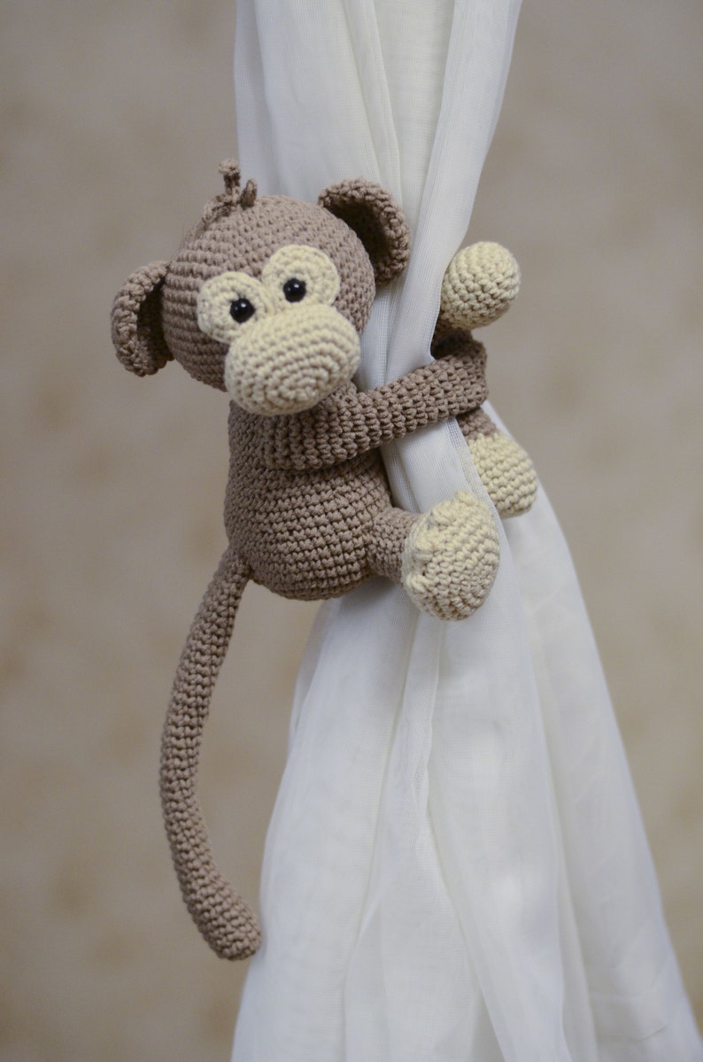 Adorable stuffed monkey curtain holder for nursery windows. Soft knitted animal decor for a newborn's room, jungle nursery accessory, and handmade gif