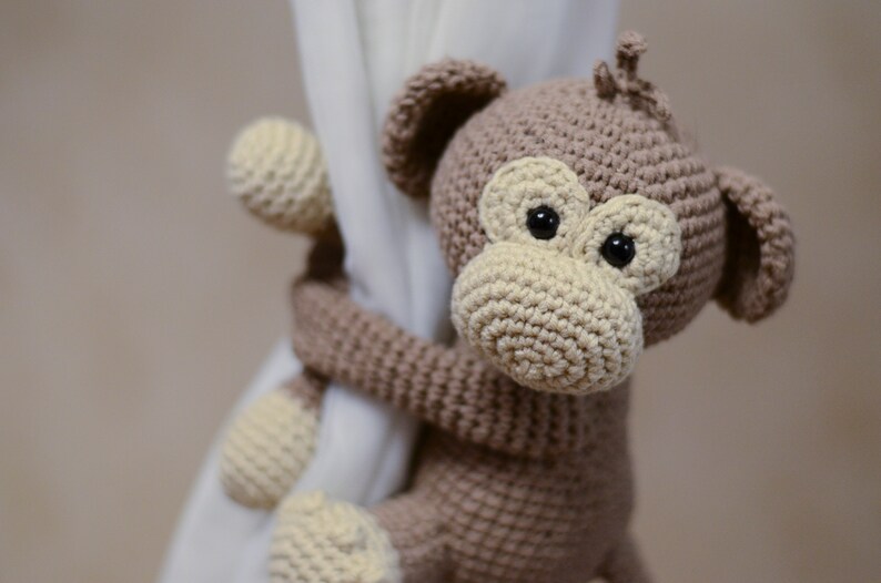 May include: A brown crocheted monkey toy with black eyes and a beige nose, holding onto a white curtain.