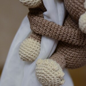 May include: A crocheted brown and cream monkey toy holding onto a white curtain. The monkey has a long tail and is holding onto the curtain with its hands.