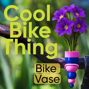 Könnte beinhalten: Ein Fahrradlenker mit einer bunten, gestapelten Vase mit lila Blumen. Die Vase ist rosa und blau, mit den Worten "Cool Bike Thing" und "Bike Vase" in gelbem Text.