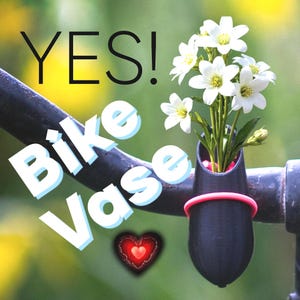Op de afbeelding: Een zwarte fietsvaas met een roze band, met witte bloemen met gele centra. De tekst "YES! Bike Vase" wordt weergegeven in wit en blauw. Er is ook een rode hartafbeelding.