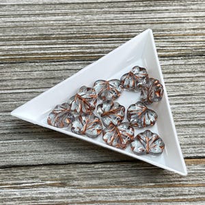May include: A collection of clear glass leaf-shaped beads with copper foil accents. The beads are arranged in a triangular white tray.