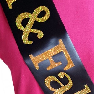 May include: Black satin sash with gold glitter lettering that reads "Bride & Groom".