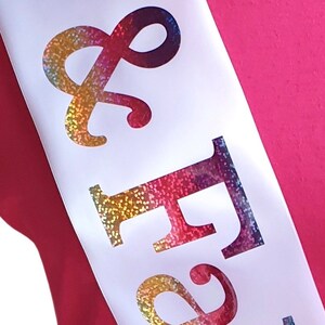 May include: White satin sash with the words "& Forever" in rainbow glitter lettering.