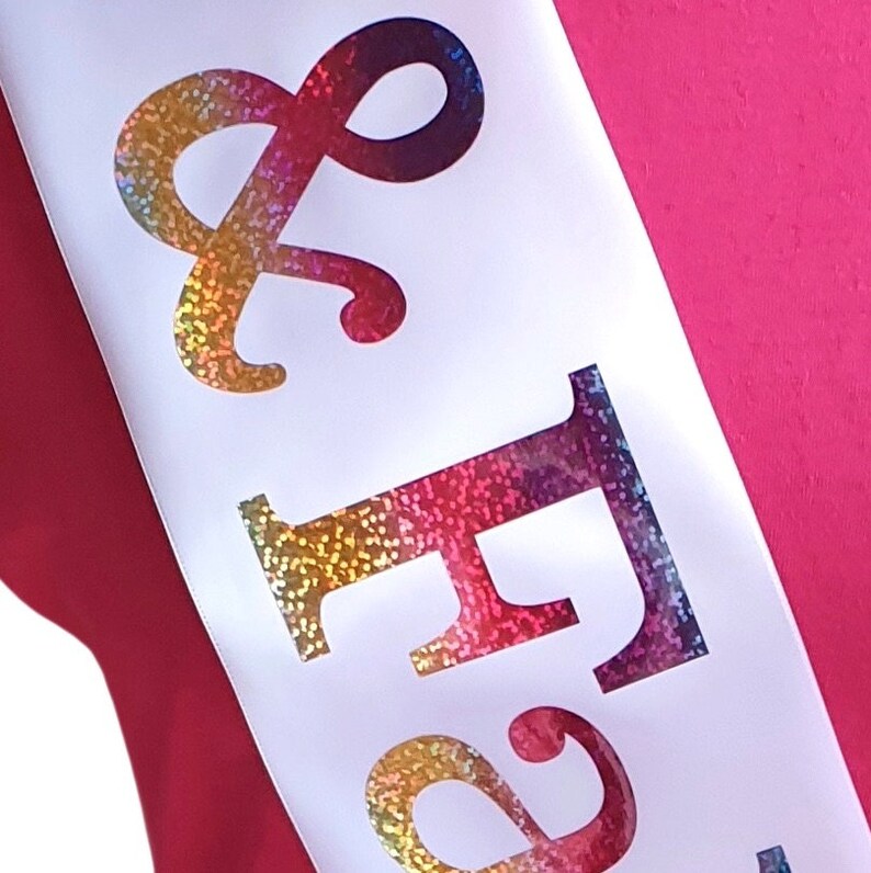 May include: White satin sash with the words "& Forever" in rainbow glitter lettering.