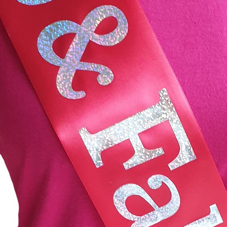 May include: Red satin sash with silver glitter lettering that reads "Bride & Groom".