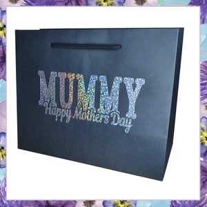 May include: A black gift bag with a holographic silver and rainbow glitter design that says "MUMMY Happy Mother's Day".
