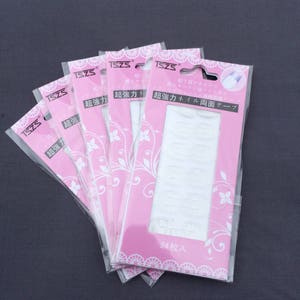 May include: Five packages of clear double-sided adhesive tape for nails. Each package is pink with white floral designs and the text "超強力ネイル両面テープ" which translates to "Super Strong Nail Double-Sided Tape".