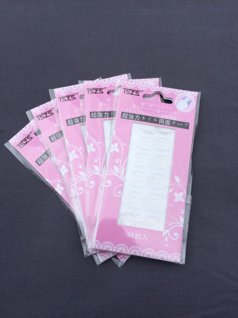 May include: Five packages of clear double-sided adhesive tape for nails. Each package is pink with white floral designs and the text "超強力ネイル両面テープ" which translates to "Super Strong Nail Double-Sided Tape".