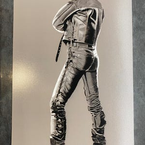 Puede incluir: Un dibujo en blanco y negro de una persona que lleva una chaqueta de cuero, pantalones vaqueros y botas. La persona est&aacute; de pie con los brazos cruzados y mirando por encima del hombro.