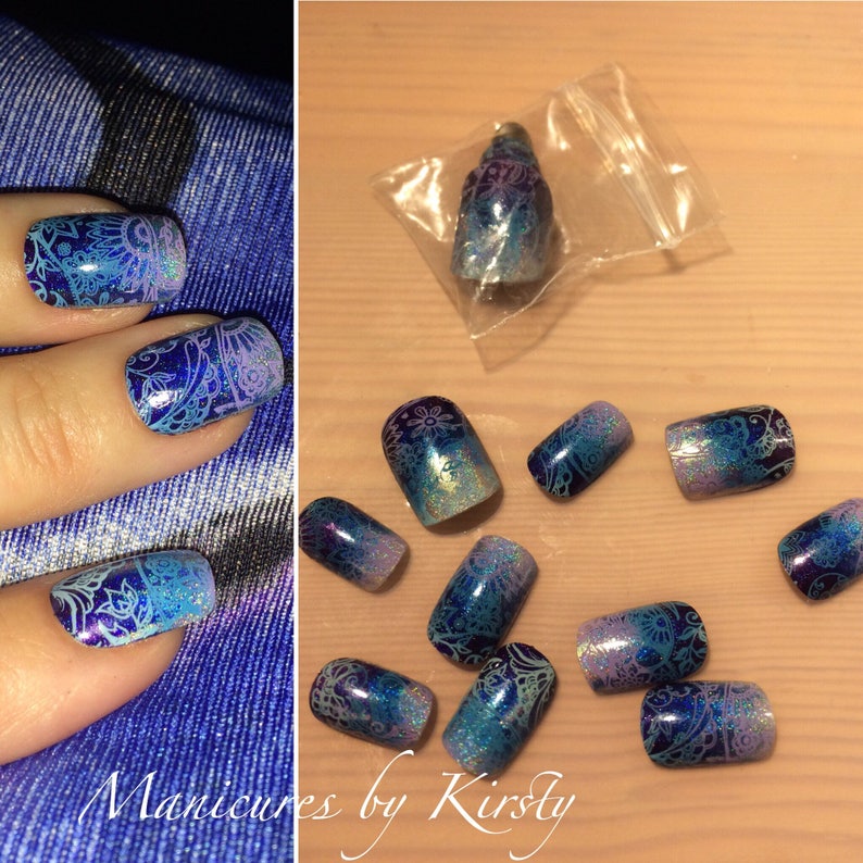 May include: A set of blue and purple ombre press-on nails with a white paisley design. The nails are packaged in a clear plastic bag.