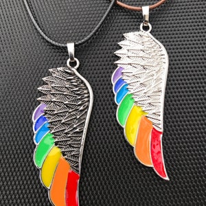 Könnte beinhalten: Zwei silberne Halsketten mit Regenbogenflügel-Anhängern. Die Flügel sind mit Federn verziert und haben eine Regenbogen-Emaille-Oberfläche.