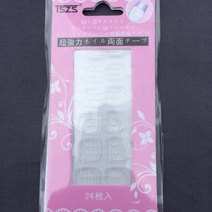 Könnte beinhalten: Eine rosa und weiße Verpackung mit 24 transparenten, selbstklebenden Nagel-Tabs. Die Verpackung enthält japanischen Text, der "超強力ネイル両面テープ" lautet, was mit "Super Strong Nail Double-Sided Tape" übersetzt wird, und "24枚入", was mit "24 Stück enthalten" übersetzt wird.