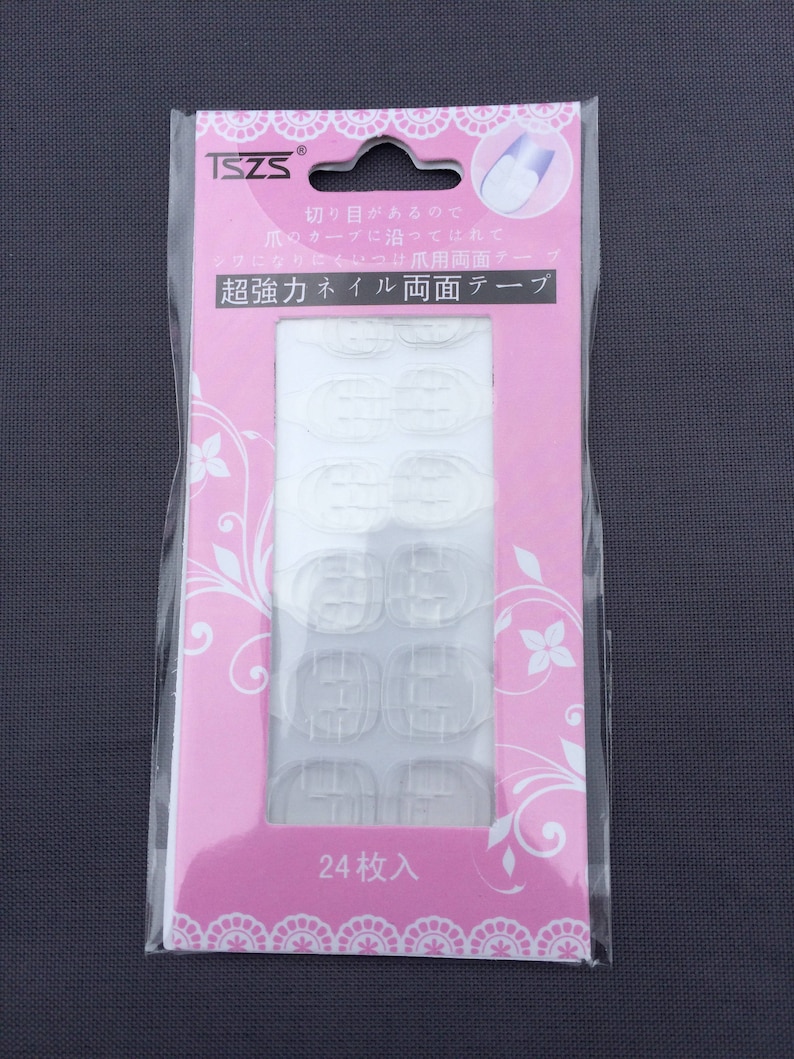 May include: A pink and white package containing 24 clear adhesive nail tabs. The package has Japanese text that reads "超強力ネイル両面テープ" which translates to "Super Strong Nail Double-Sided Tape" and "24枚入" which translates to "24 pieces included".