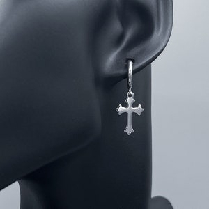 May include: Silver cross dangle earring on a mannequin's ear. The earring is a simple, classic design.