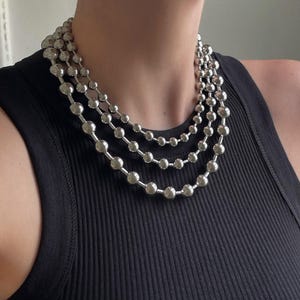 Peut inclure: Un collier en cha&icirc;ne argent avec trois rangs de gros perles rondes.