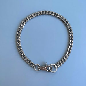 Puede incluir: Un collar de cadena de plata con un cierre de plata. La cadena es de estilo curb.