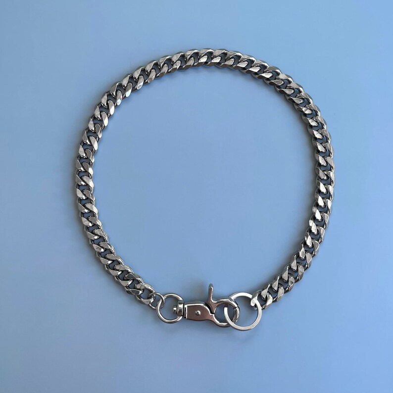 Puede incluir: Un collar de cadena de plata con un cierre de plata. La cadena es de estilo curb.