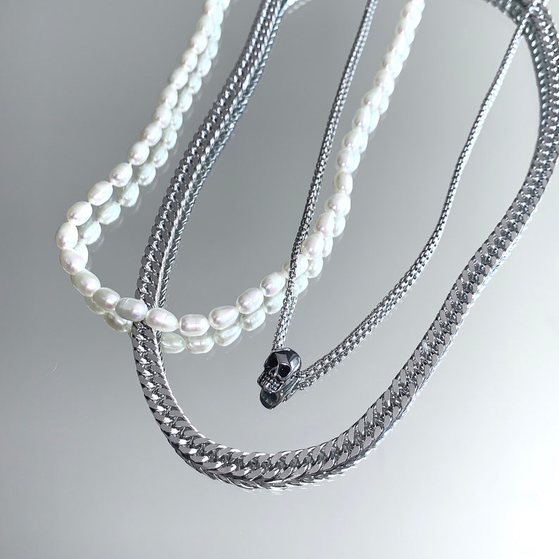 Puede incluir: Un collar de capas con una cadena de plata y una hebra de perlas. La cadena tiene un peque&ntilde;o colgante de calavera negra.