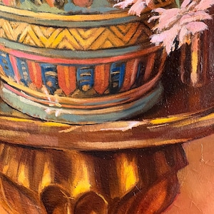 May include: A decorative ceramic pot with a geometric pattern in shades of yellow, blue, red, and brown. The pot is filled with pink flowers and sits on a wooden stand with a gold finish.