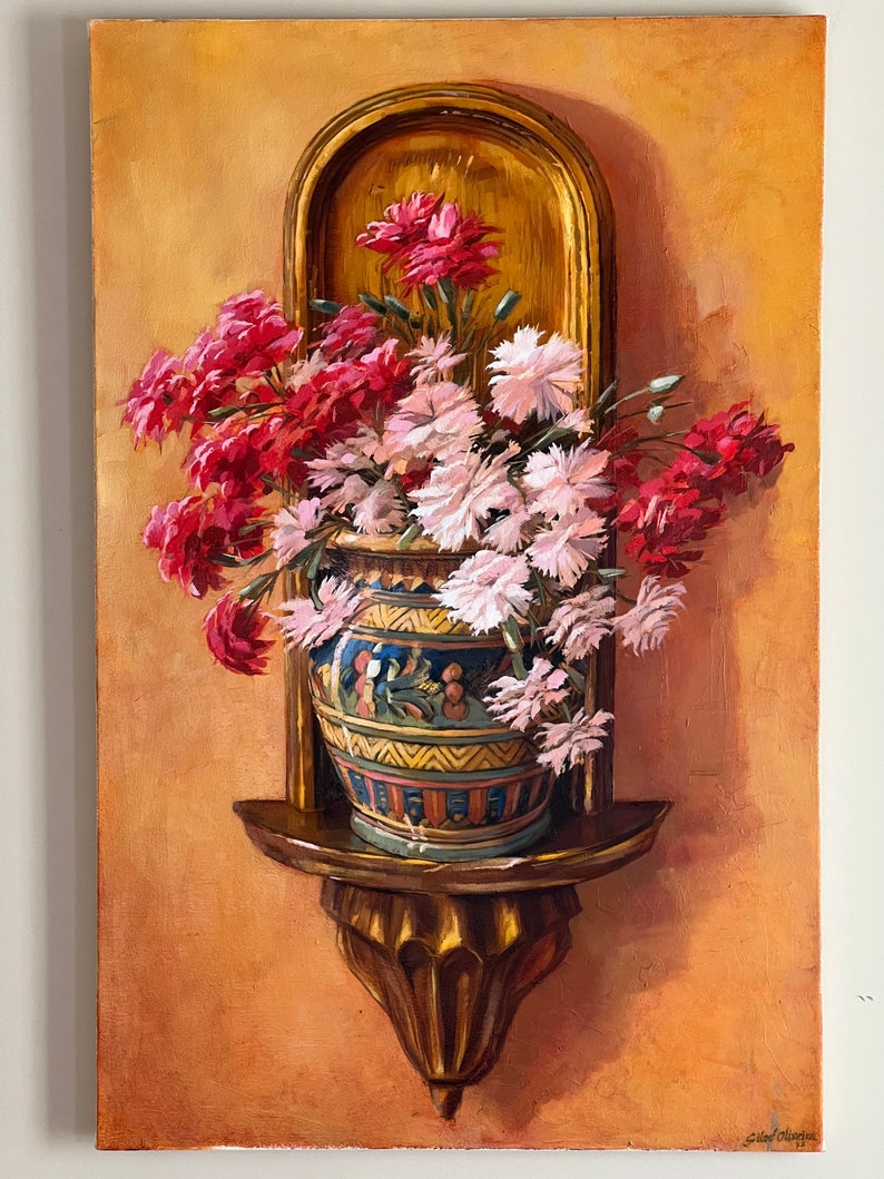 May include: A painting of a bouquet of pink and red carnations in a decorative ceramic vase on a wooden shelf. The shelf is attached to a wall with a gold frame.