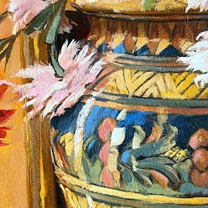 May include: A close-up of a pink and white flower arrangement in a large, ornate, yellow and blue ceramic vase. The vase has a geometric pattern and is decorated with a floral motif.