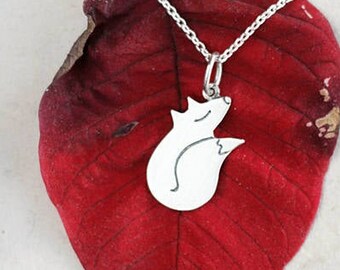 Könnte beinhalten: Eine silberne Halskette mit einem kleinen, eingerollten Fuchs-Anhänger. Die Kette liegt auf einem roten Blatt.