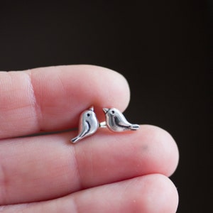 Peut inclure: Une paire de boucles d'oreilles en argent en forme d'oiseau. Les oiseaux se font face et mesurent environ la taille d'une pièce de 10 centimes.