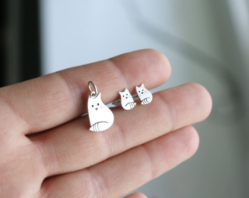 Puede incluir: Un conjunto de pendientes de plata con forma de gato y un collar con un colgante de plata con forma de gato. Los dijes con forma de gato son simples y minimalistas, con un dise&ntilde;o lindo de estilo de dibujos animados.