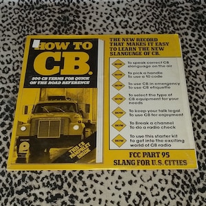 May include: A yellow and black book titled "How to CB" with a picture of a semi-truck on the cover. The book includes 500 CB terms for quick on-the-road reference. The book also includes a pamphlet inside with information about CB slang.