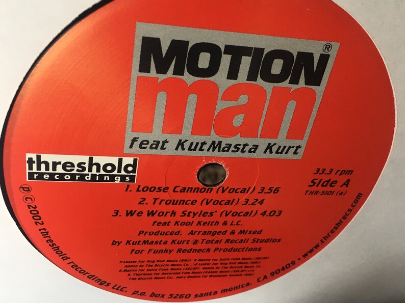 May include: A red vinyl record with a white label. The label has black text that reads "MOTION man feat Kut Masta Kurt" and "threshold recordings". The track list includes "Loose Cannon (Vocal)", "Trounce (Vocal)", and "We Work Styles (Vocal)".