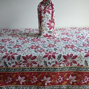 May include: A fabric drawstring bag and a matching rectangular tablecloth, both featuring a white background with a repeating pattern of red poinsettia flowers, green holly leaves, and small yellow berries, finished with a decorative red border.