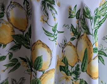 May include: White tablecloth with a lemon print. The lemons are yellow with green leaves and stems. The background is white with a subtle texture.