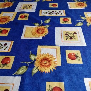 May include: A blue tablecloth with a repeating pattern of sunflowers, olives, and tomatoes. The sunflowers are yellow and orange, the olives are black, and the tomatoes are red. The tablecloth has a textured appearance.