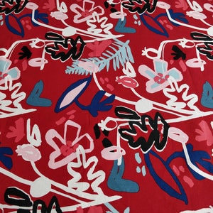 May include: Red fabric with a repeating floral pattern. The design features stylized flowers and leaves in white, black, pink, light blue, and dark blue. The overall aesthetic is modern and artistic, suitable for various textile applications.