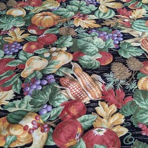 Könnte beinhalten: Ein Stoff mit einem farbenfrohen Erntethema. Das Design zeigt Kürbisse, Mais, Äpfel, Trauben, Birnen und Blätter in Orange-, Rot-, Grün- und Lilatönen. Der Hintergrund ist ein dunkles Marineblau.