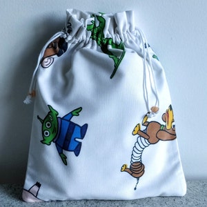 May include: White drawstring bag featuring colorful cartoon character illustrations. The bag has a cinched top with a white drawstring and wooden bead accents. The bag is made of a soft fabric.