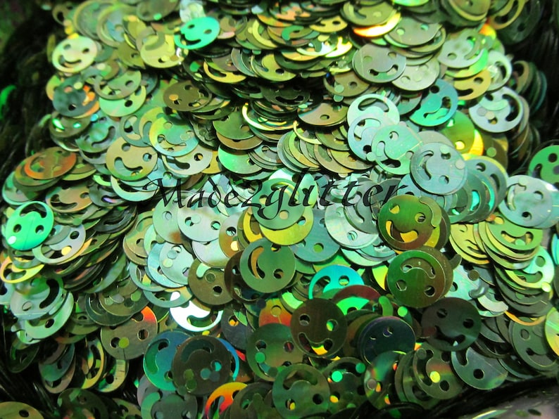 Op de afbeelding: Een close-up afbeelding van een grote stapel groene, iriserende glitter in de vorm van smiley's.