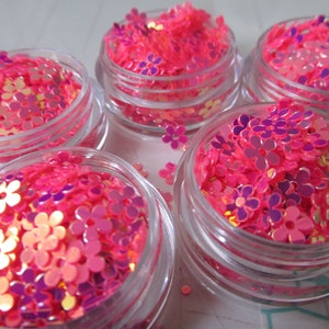 May include: Four small glass jars filled with pink and gold iridescent flower-shaped glitter.